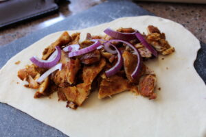 Vul het gerolde pizzadeeg met shoarma en rode ui